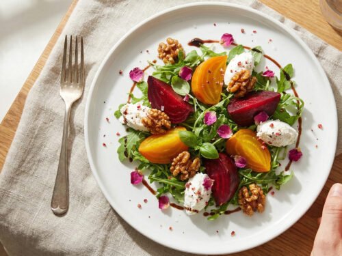 one-hand friendly beet and goat cheese ruby salad with arugula, walnuts, and balsamic-rose drizzle on a white plate one-hand friendly beet and goat cheese ruby salad with arugula, walnuts, and balsamic-rose drizzle on a white plate